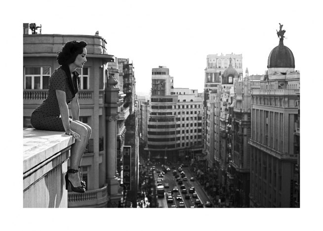 Sort-hvidt fotografi af kvinde, der kigger ned på bygen fra et tag