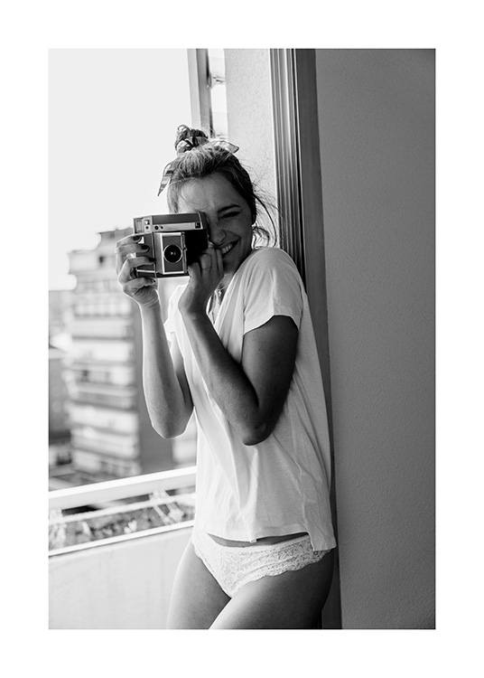 Sort-hvidt fotografi af smilende kvinde, der holder et kamera, iført hvid T-shirt