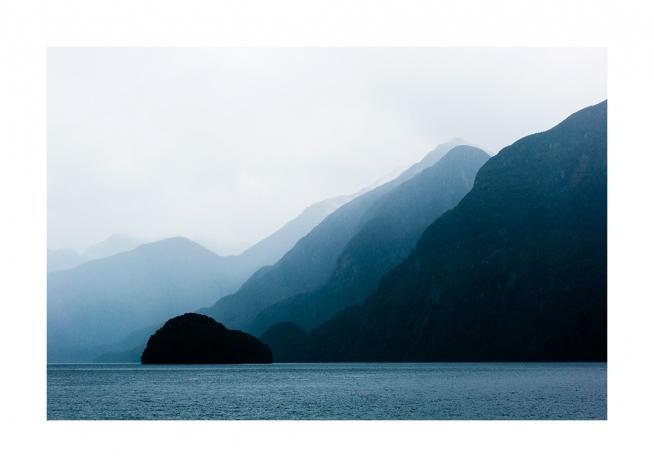  - Fotografi af hav foran en række bjerge med tåge bag