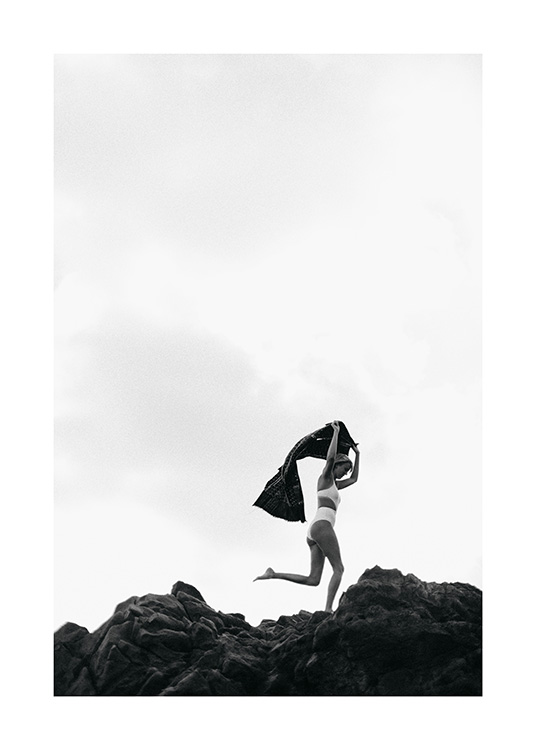  - Sort-hvid fotografi af en kvinde i hvid bikini, der løber over nogle klipper, mens hun holder et håndklæde over hovedet