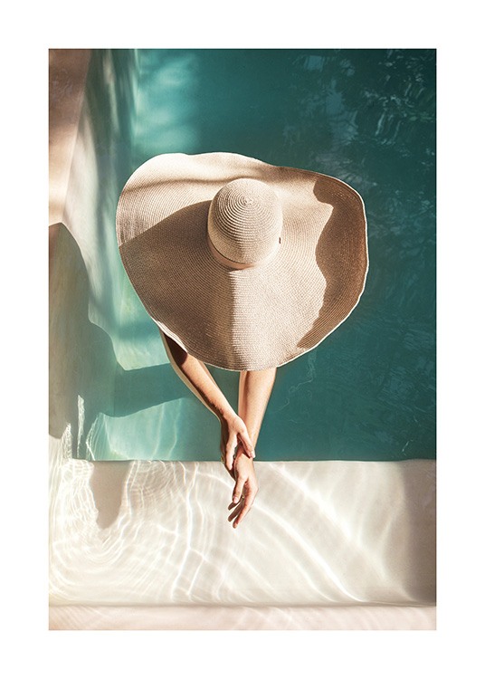  – Fotografi af en kvinde i en solhat, der står i en swimmingpool med armene strakt ud foran sig