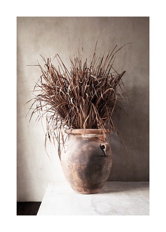  – Fotografi af tørret, beige græs i en vase mod en beige betonvæg