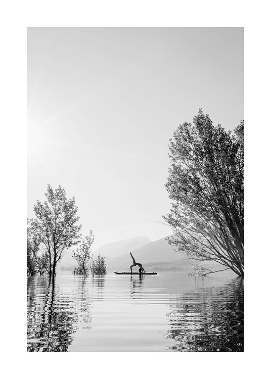  – Sort-hvidt fotografi af en kvinde i yogastilling på et surfbræt i midten af en sø