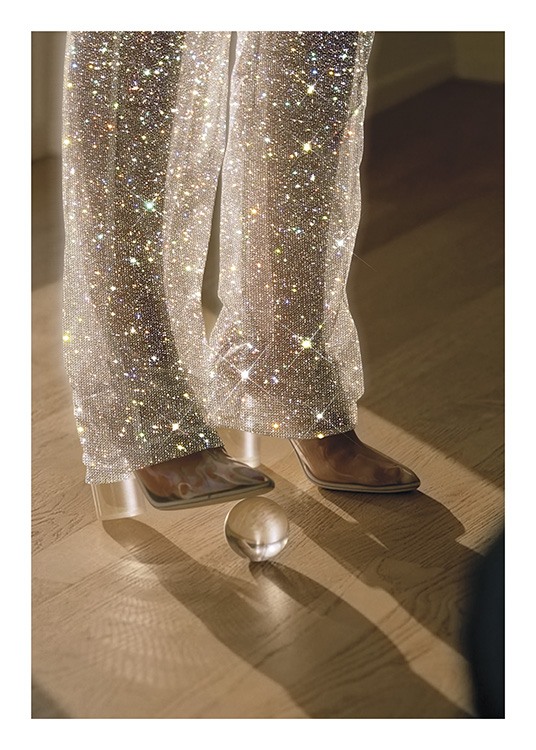  – Fotografi af en kvinde med en glaskugle under sin højhælede sko iført glitrende bukser