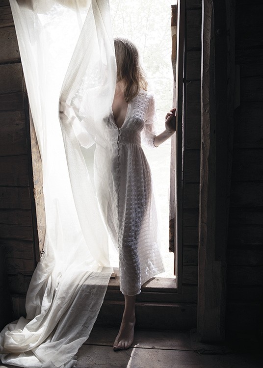  – Fotografi af en kvinde iført en hvid kjole i en døråbning, der er dækket af et hvidt gardin
