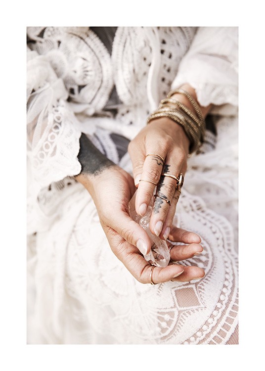  – Fotografi af hænder, der holder en krystal, med guldsmykker og en hvid blondekjole i baggrunden