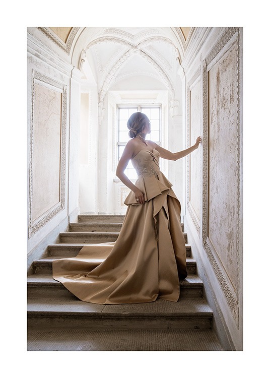  – Fotografi af en kvinde iført en beige og gylden kjole, der står på en trappe i barokstil