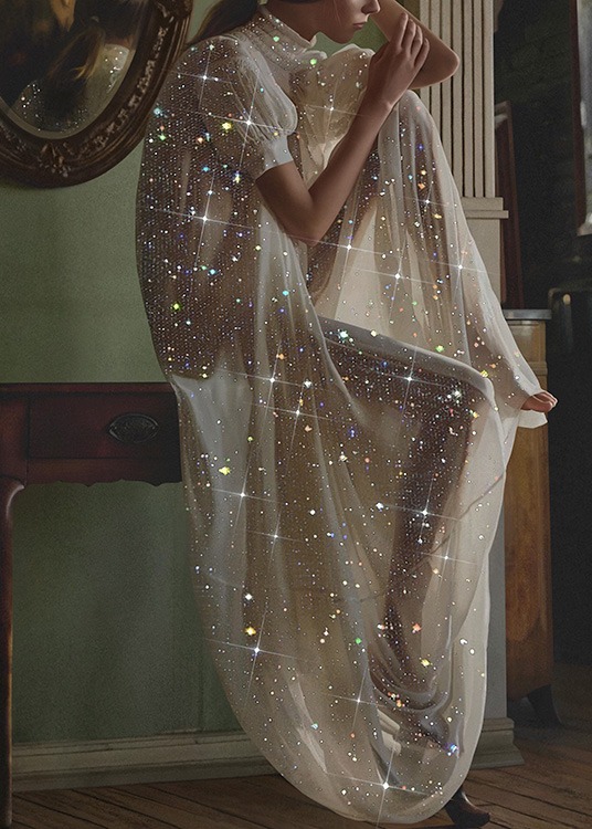  – Fotografi af en kvinde iført en hvid, gennemsigtig kjole med glimmer, der sidder på et skrivebord