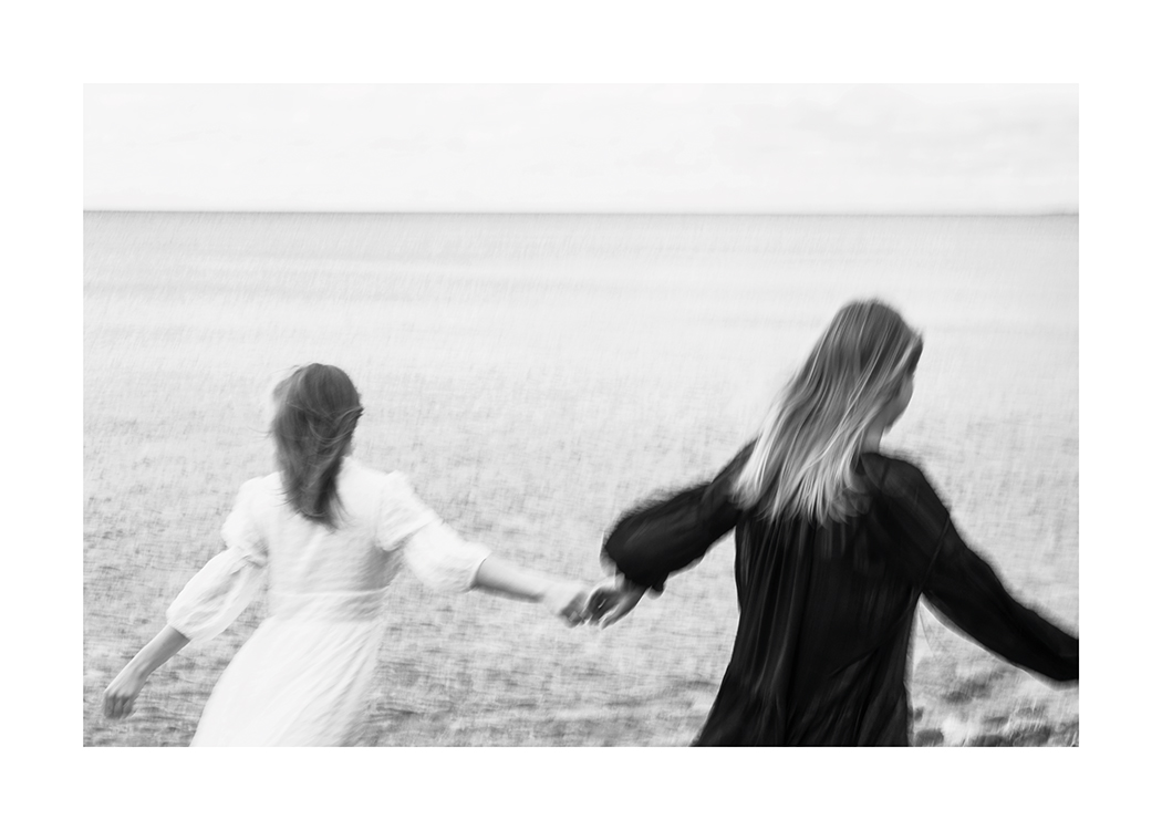  – Sort-hvidt foto af to kvinder, der løber over en eng, mens de holder hinanden i hånden