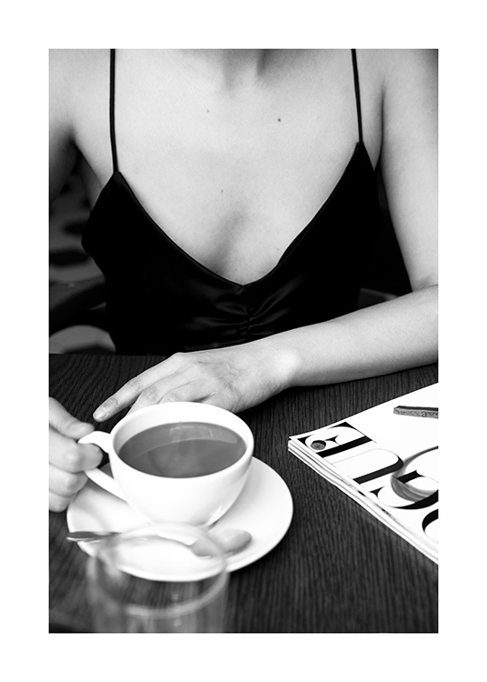 –- Sort-hvidt fotografi af en kvinde, der sidder ved et cafébord med en kop kaffe på bordet